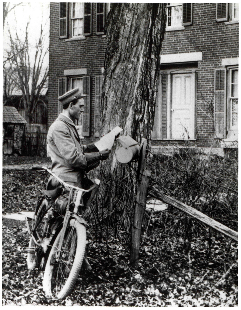 Photograph of letter carrier delivering mail by bicycle
